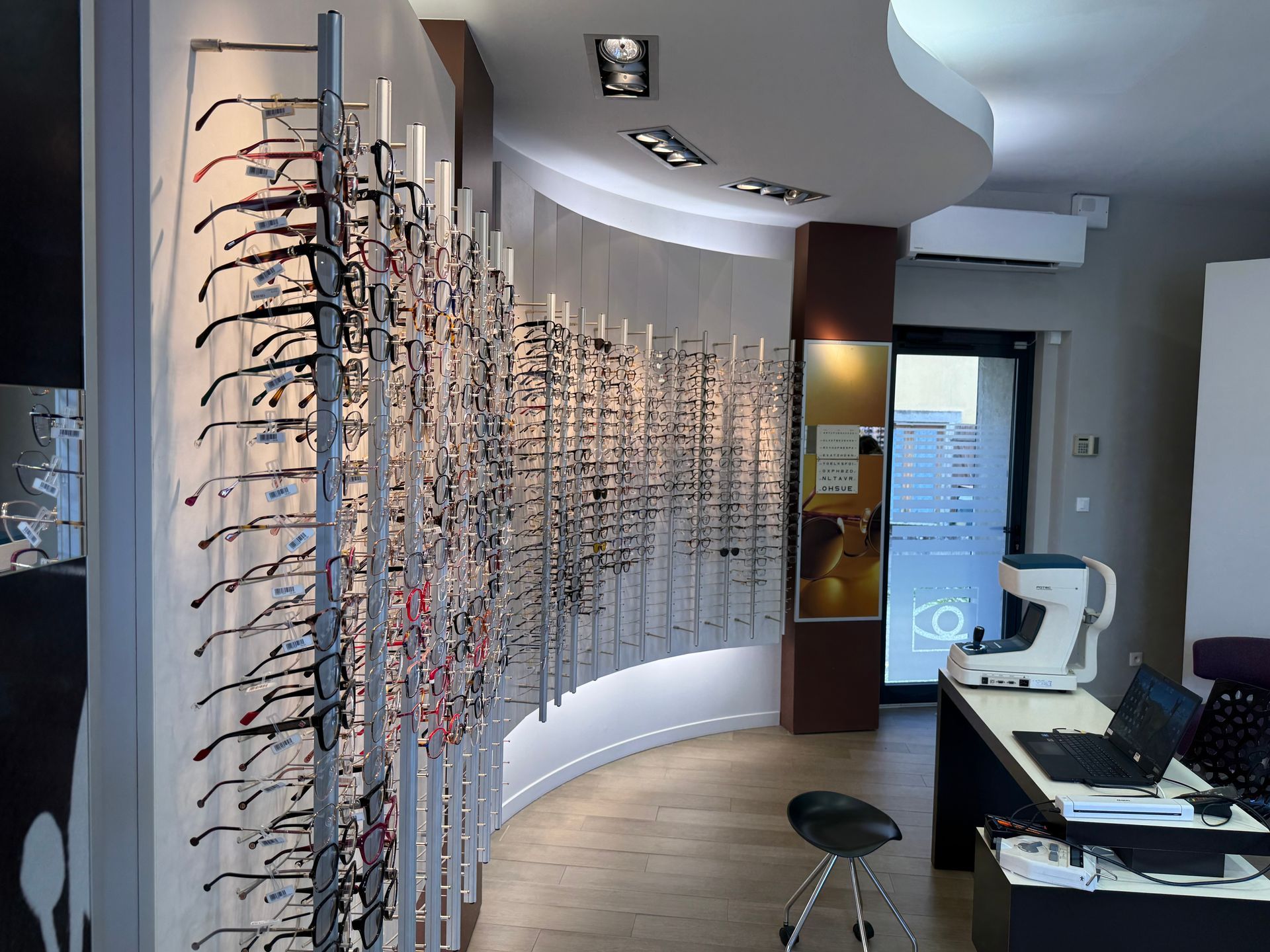 Intérieur d'un magasin d'optique : un mur incurvé présente des lunettes.