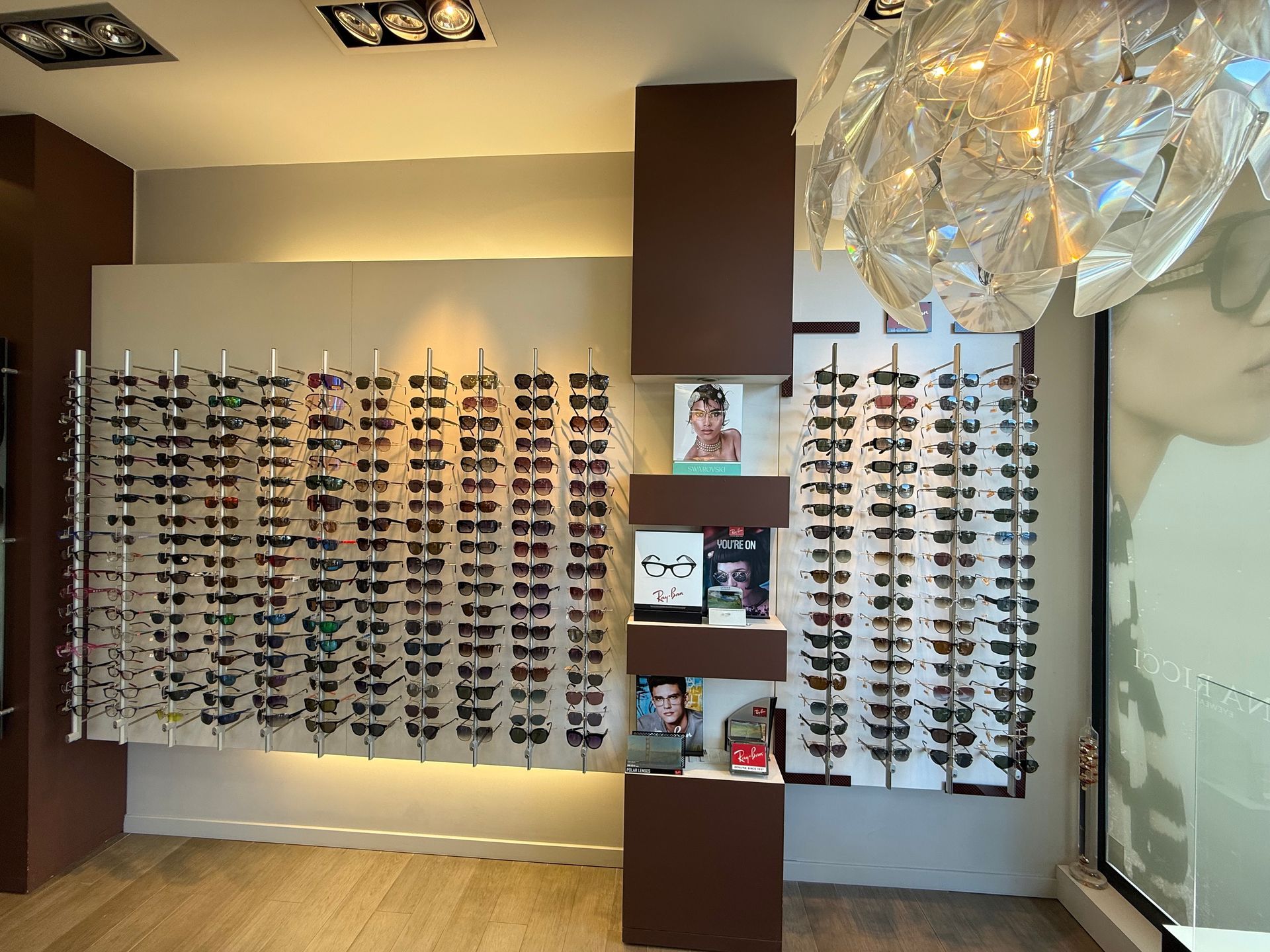Lunettes de soleil exposées dans un magasin d'optique. Des présentoirs muraux mettent en valeur de nombreuses montures.
