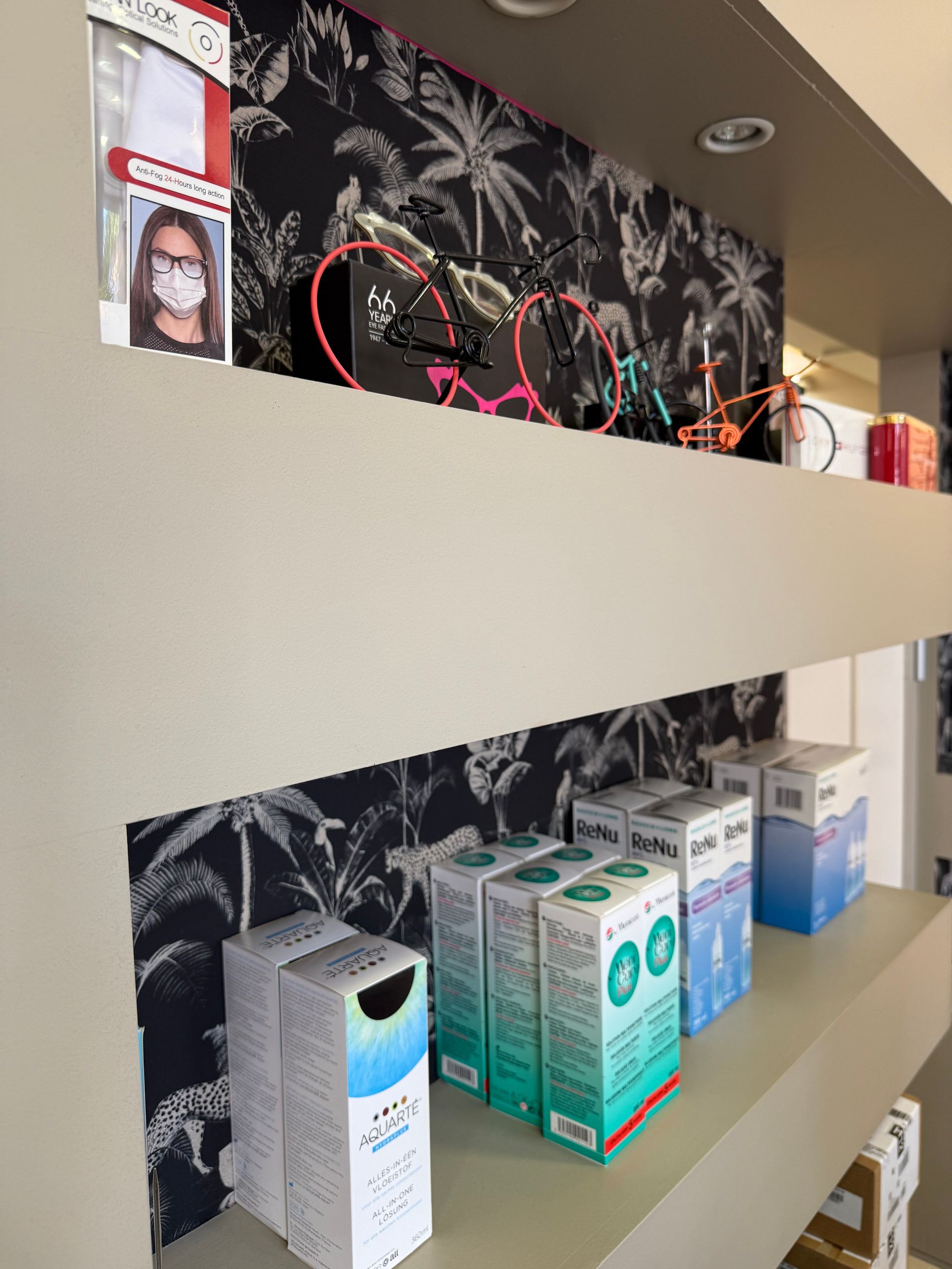 Des étagères présentent des produits de soins oculaires, sur un papier peint noir à motifs tropicaux.