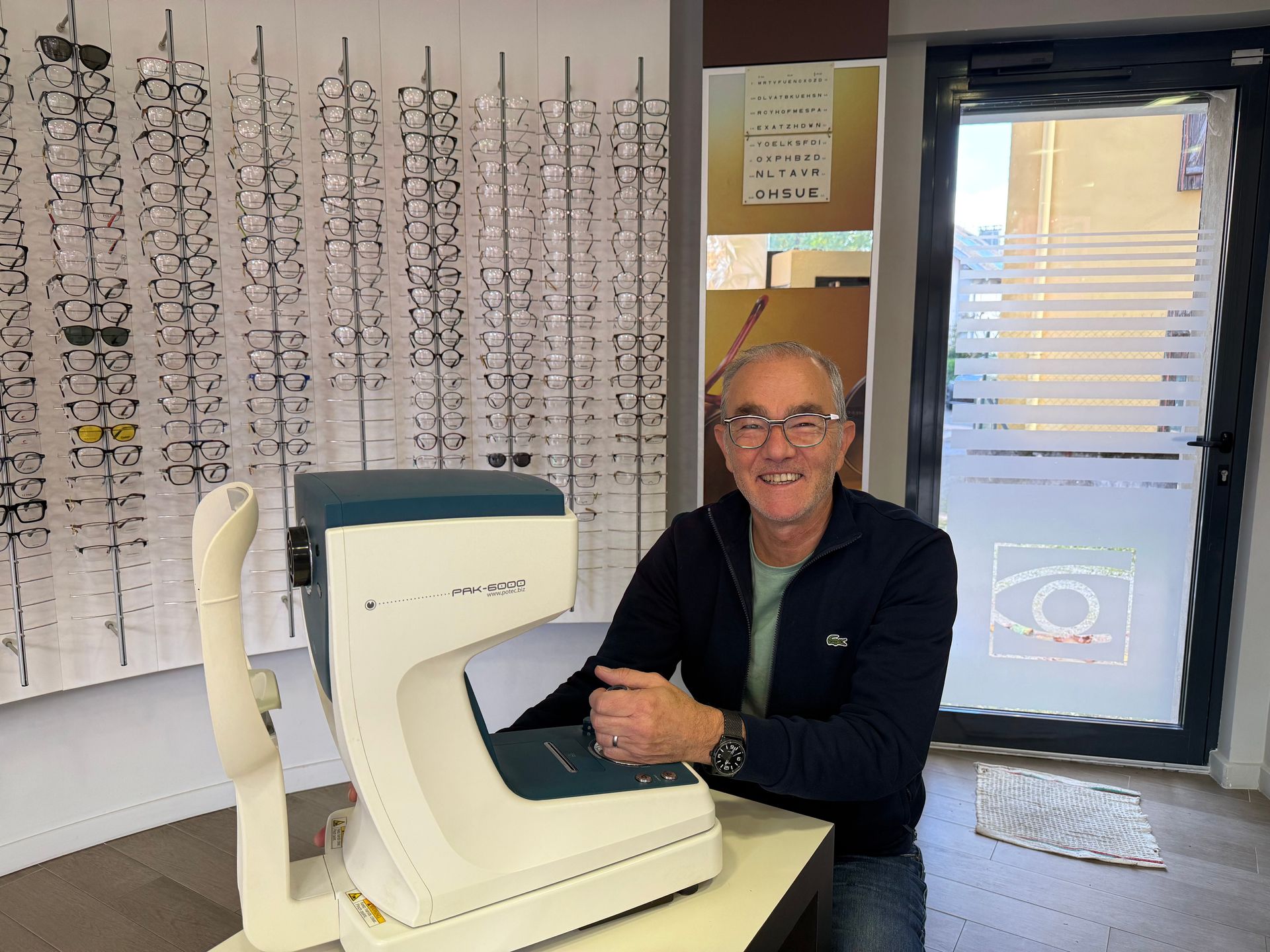 M. Rondot dans sa boutique d'optique, devant une machine pour les contrôles de vue. Il sourit.