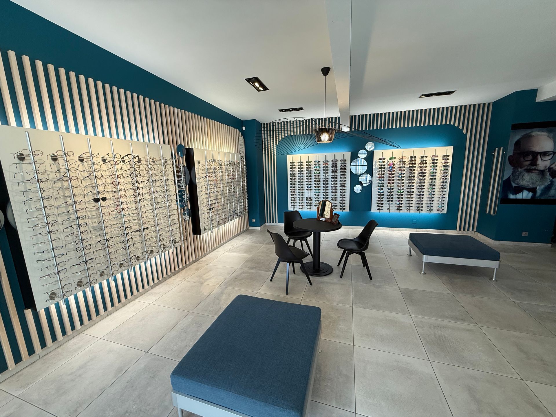 L'intérieur d'un magasin d'optique avec des présentoirs à lunettes, des murs bleus, des sièges et une petite table.