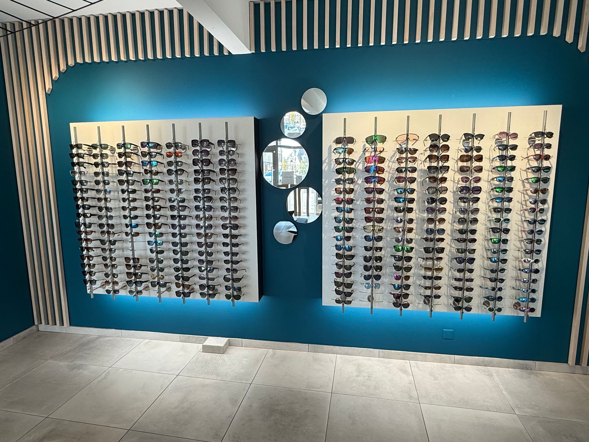 Des lunettes de soleil présentées sur deux tableaux blancs devant un mur turquoise orné de miroirs.