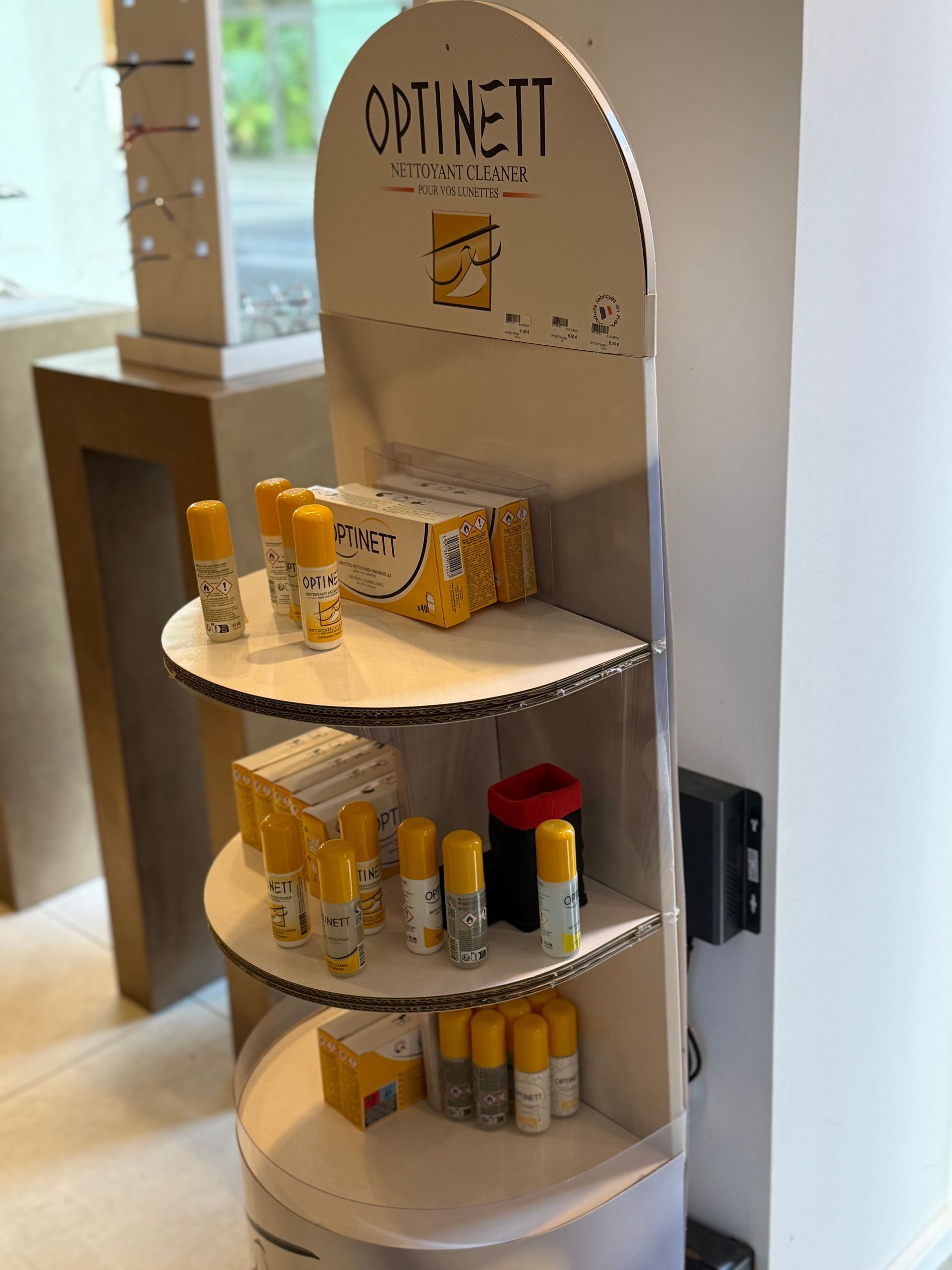 Présentoir avec produits de soins oculaires Optinett : jaune, blanc et gris, dans un magasin.