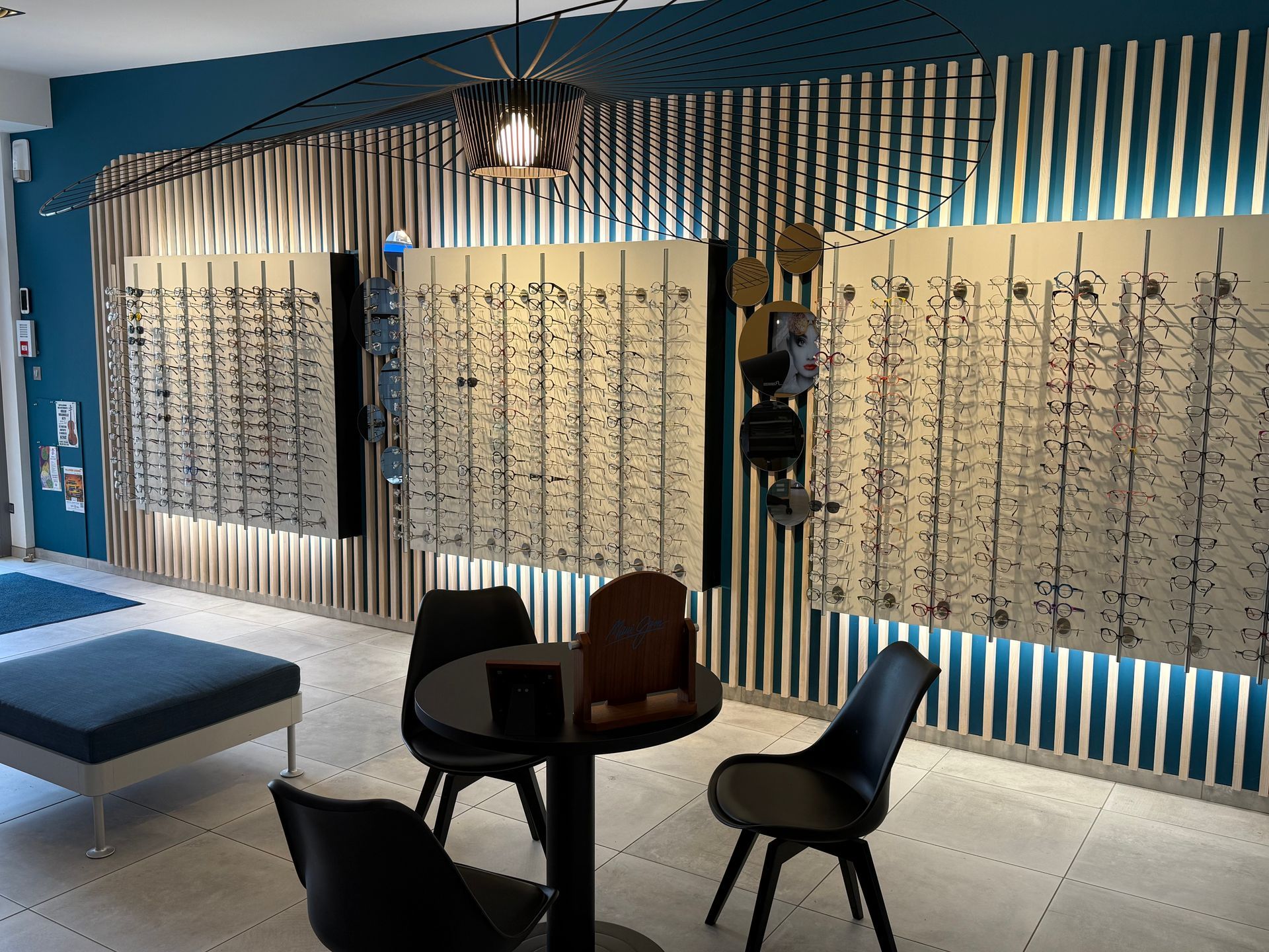 Dans le showroom d'un opticien, des montures de lunettes sont exposées sur un mur orné de boiseries et de rayures.