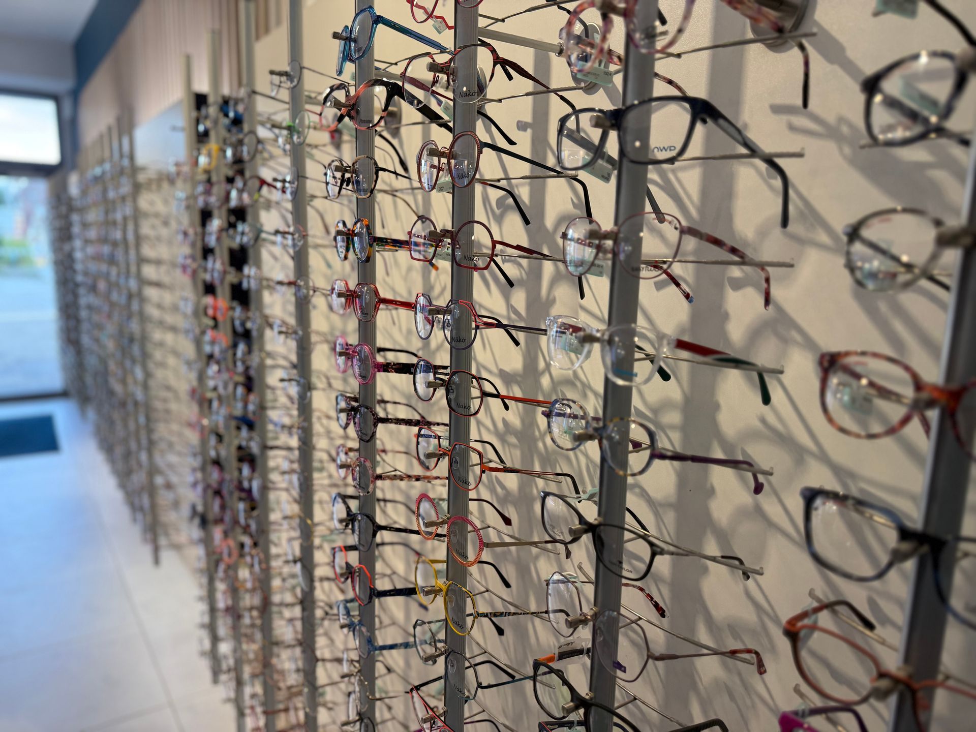 Présentoir mural de lunettes dans un magasin, avec différents styles et couleurs de montures.