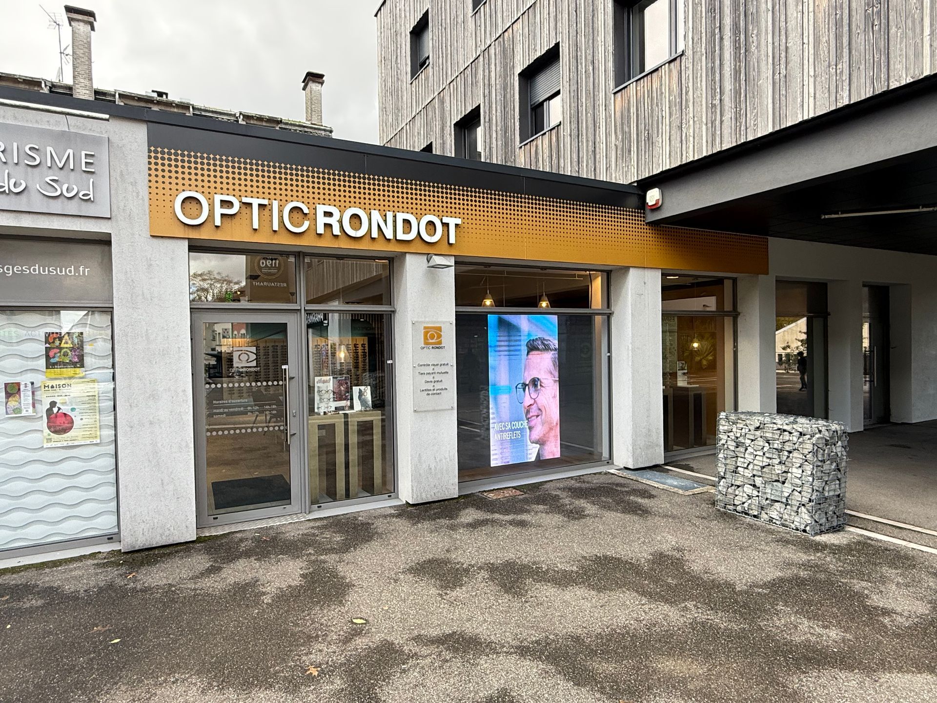 Façade du magasin Optic Rondot avec enseigne dorée, vitrines et façade en pierre.