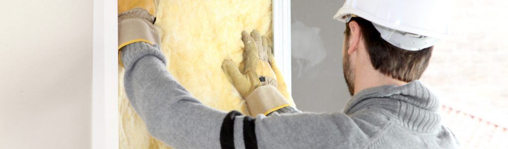 Une personne portant un casque et des gants installe de l'isolant dans un mur.