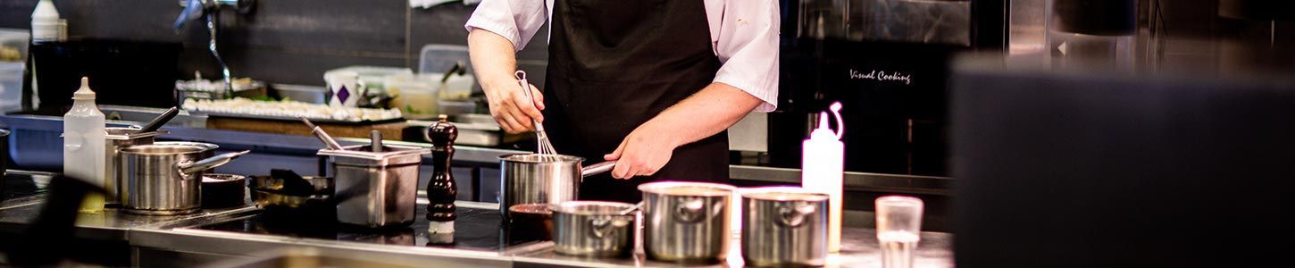 Un chef cuisinier, dans une cuisine professionnelle, mélange des ingrédients dans une casserole sur la plaque de cuisson.