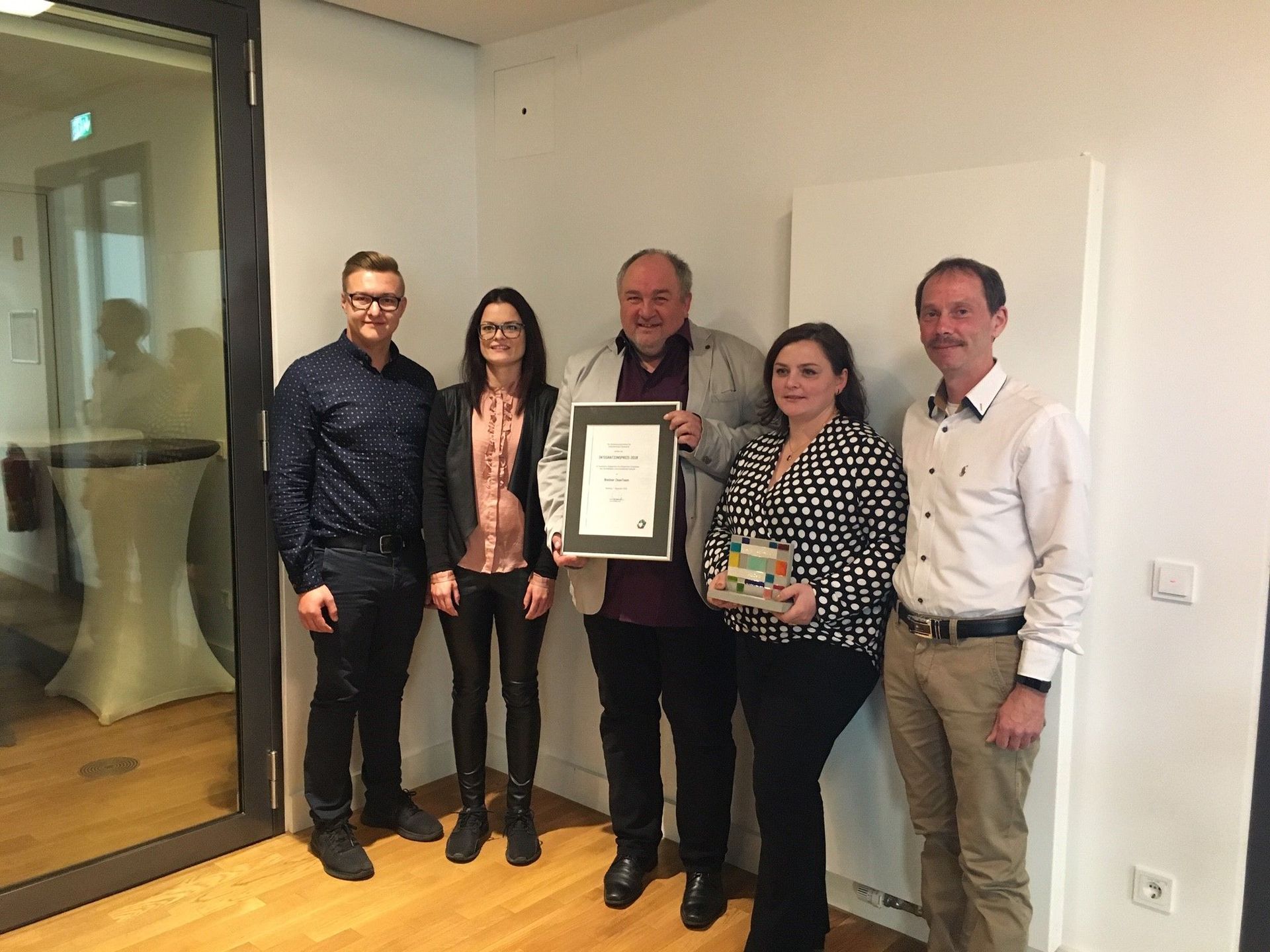 Eine Gruppe von Menschen steht in einem Raum nebeneinander und hält ein Zertifikat in den Händen.