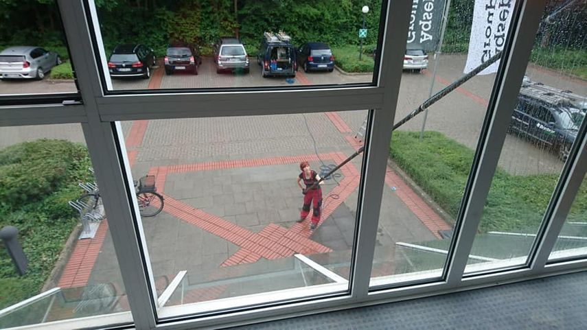 Ein Mann putzt auf einem Parkplatz mit einem Schlauch ein Fenster.