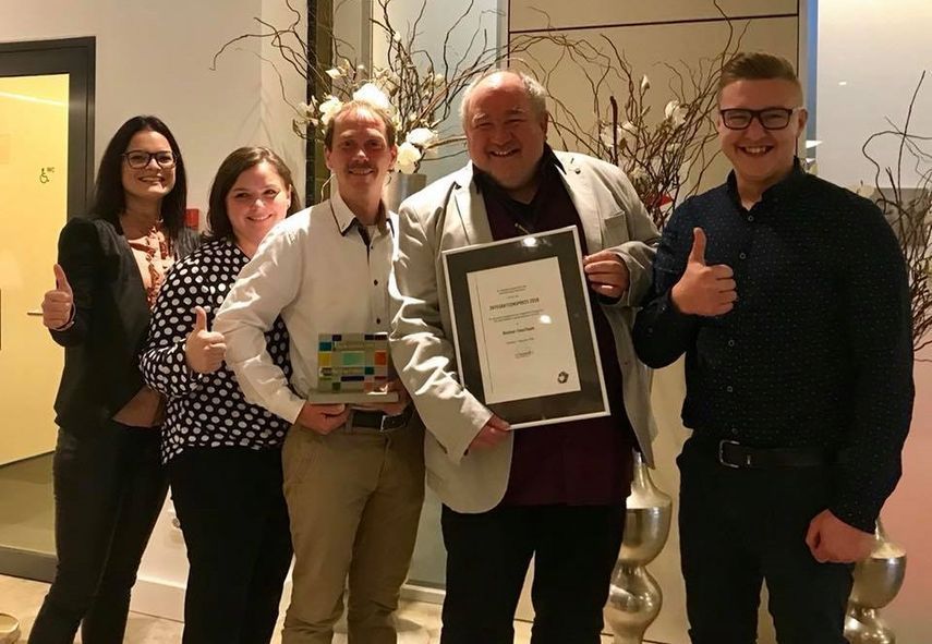 Eine Gruppe von Menschen posiert für ein Foto und einer von ihnen hält eine Urkunde in der Hand.