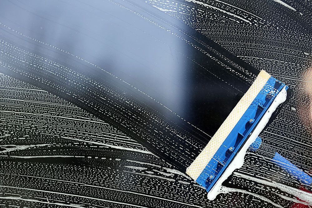 Eine Person reinigt ein Fenster mit einem Abzieher.