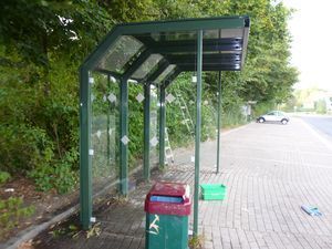 Eine Bushaltestelle mit einem grünen Vordach und einem roten Mülleimer.