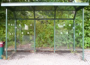 Eine Bushaltestelle mit Glasdach und einem Mülleimer davor.