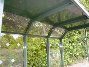 Eine Bushaltestelle mit Glasdach und Bäumen im Hintergrund.