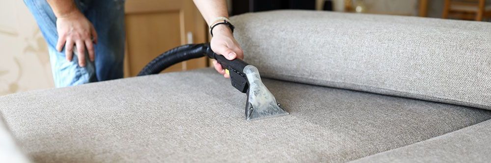 Eine Person reinigt ein Sofa mit einem Staubsauger.