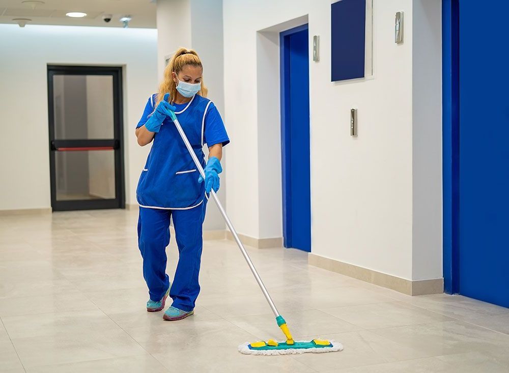 Eine Frau mit Maske und Handschuhen reinigt den Boden mit einem Mopp.