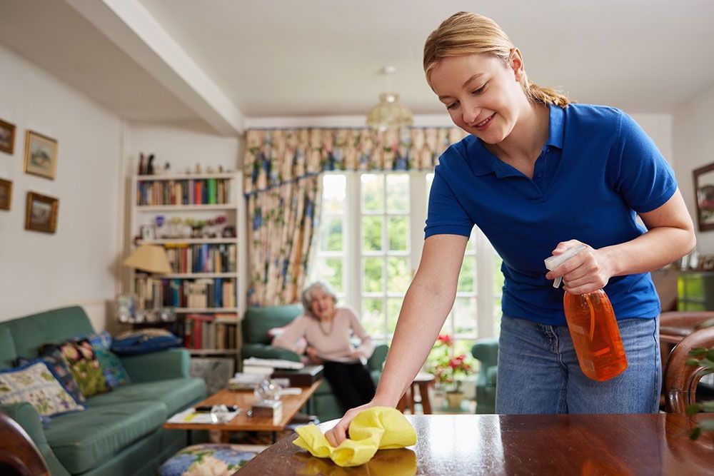 Eine Frau in einem blauen Hemd reinigt einen Tisch in einem Wohnzimmer.