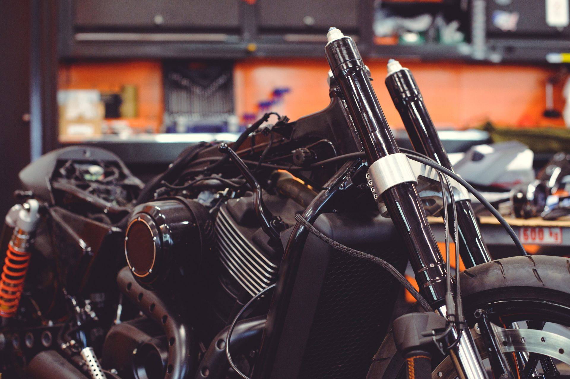 Motocicleta negra en reparación en un garaje, con horquillas delanteras y amortiguadores naranjas.