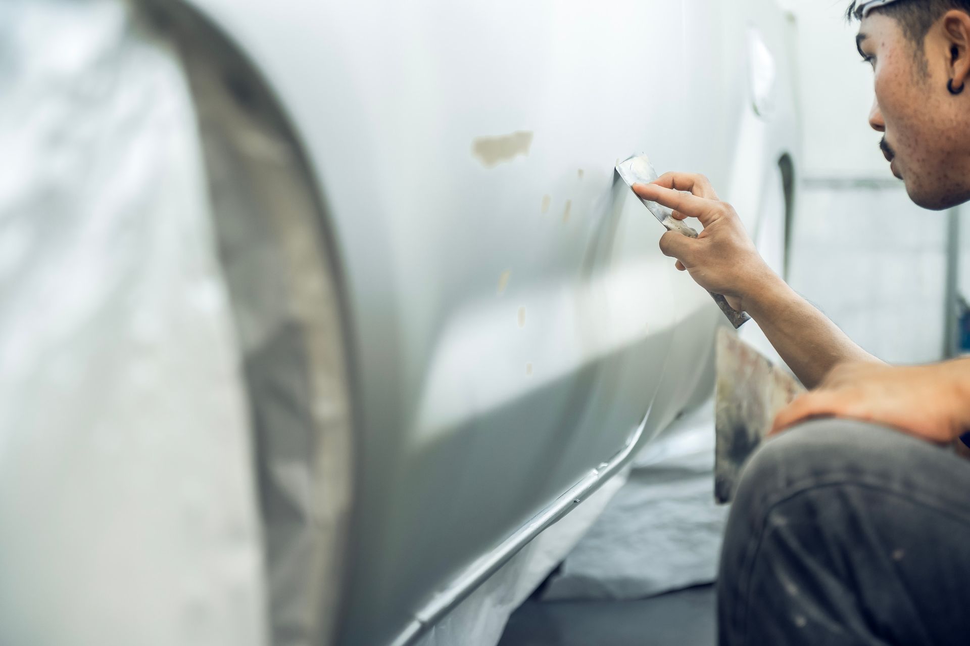 Persona reparando la puerta de un coche. Utilizando una herramienta para alisar la carrocería de un coche blanco.