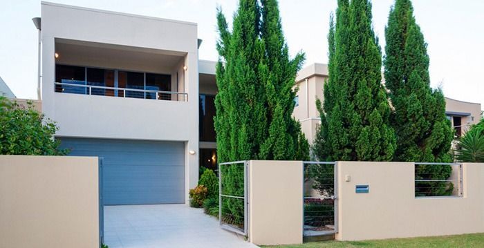 Una casa moderna con una puerta de garaje azul y árboles delante de ella.