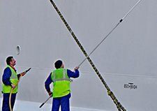 Dos trabajadores con monos azules y chalecos de seguridad limpian una gran estructura blanca con postes.