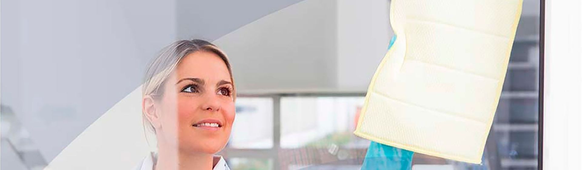 Mujer sonriendo mientras limpia una ventana. Tela beige enmarcada.