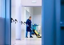 Una persona con uniforme azul aspira un pasillo luminoso con productos de limpieza.