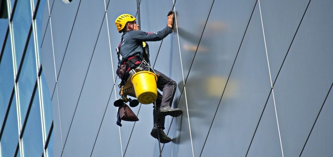 Limpiacristales suspendido por cuerdas, limpiando la fachada de cristal de un edificio de gran altura.