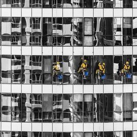 Limpiadores de ventanas con trajes amarillos limpiando un edificio de cristal. Cristal reflectante en blanco y negro.