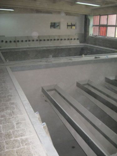 Interior de un lavabo de hormigón con múltiples grifos, probablemente un lavadero público.