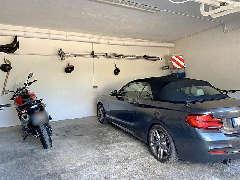 Un coche descapotable azul oscuro y una motocicleta roja estacionados dentro de un garaje.
