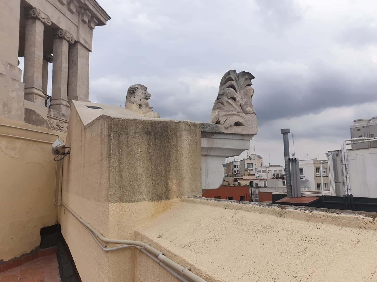 Vista desde la azotea con esculturas de leones desgastados, cielo nublado y edificios de la ciudad.