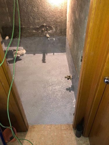 Vista desde la puerta hacia una habitación pequeña y oscura con piso recién revestido y tuberías expuestas.