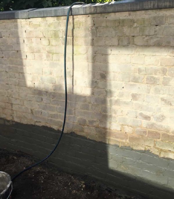 Pared de ladrillo con una línea oscura de mortero en la base y una manguera que baja.