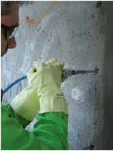 Persona con equipo de seguridad utilizando un taladro en una pared de hormigón.