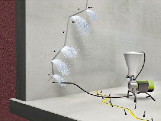Una máquina proyecta hormigón sobre una pared. Tubería gris con cabezales de ducha. Tanque y bomba blancos. Cable amarillo.