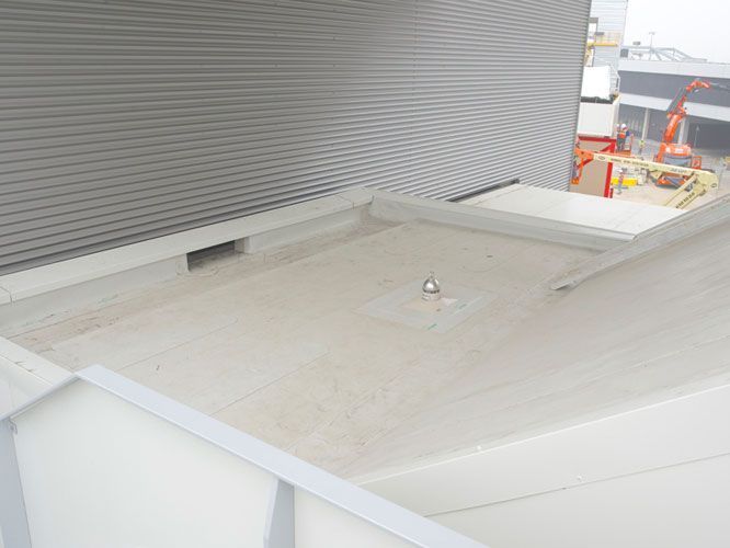 Techo plano con drenaje, adosado a un edificio de chapa ondulada.