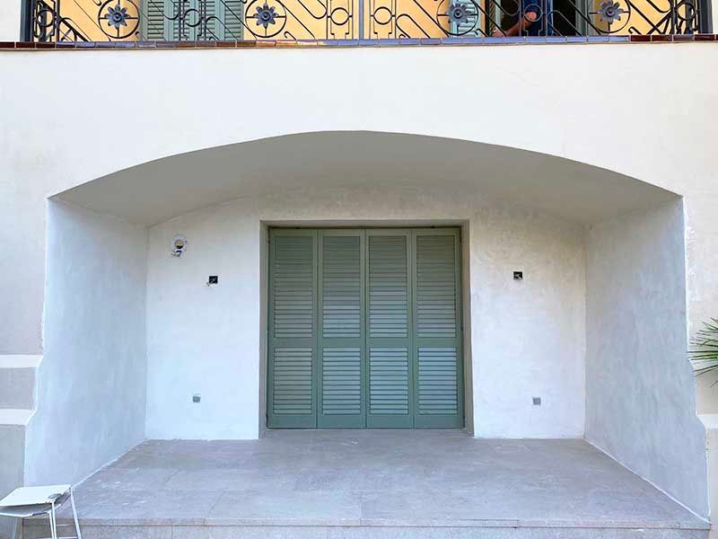Puerta con contraventanas verdes empotrada en un nicho arqueado en un edificio blanco.