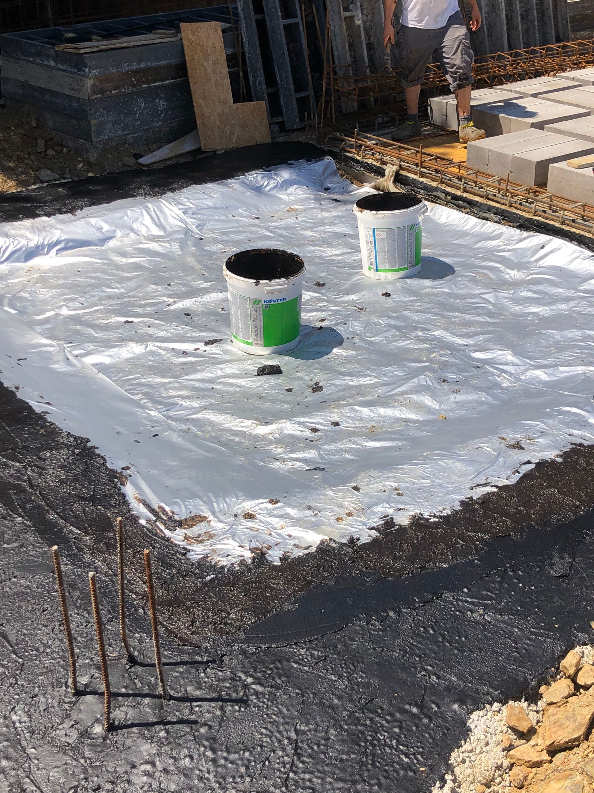 Obra: Dos cubos sobre una lona blanca dentro de una base oscura. Se ven varillas de refuerzo y materiales de construcción.