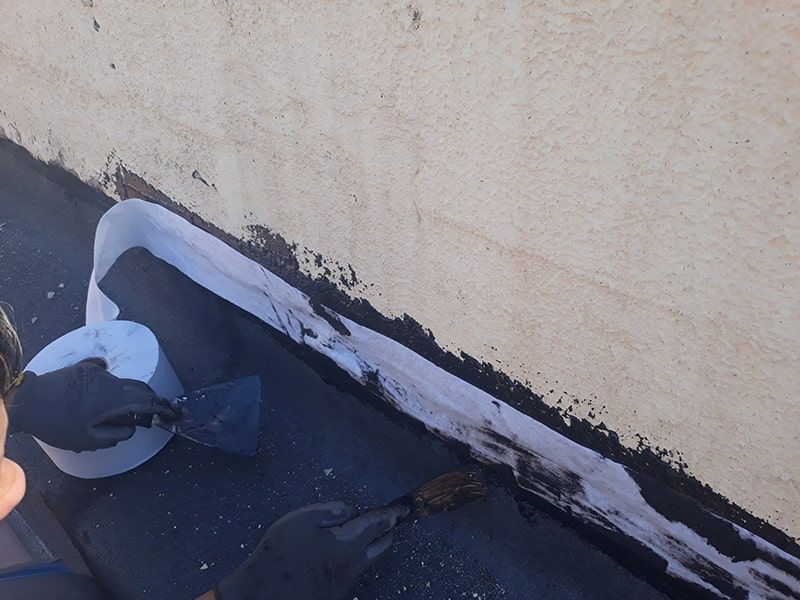 Persona aplicando sellador a lo largo del borde de un techo contra una pared, usando una paleta.