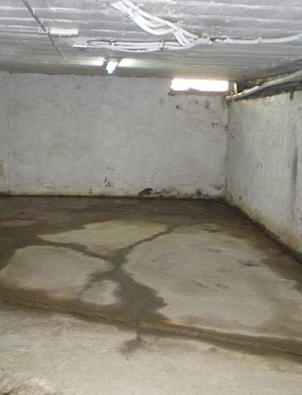 Suelo de sótano con manchas de agua, paredes húmedas y una pequeña ventana.