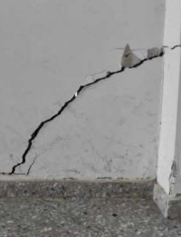 Pared agrietada, línea diagonal negra, esquina de un edificio, base gris, pared blanca.