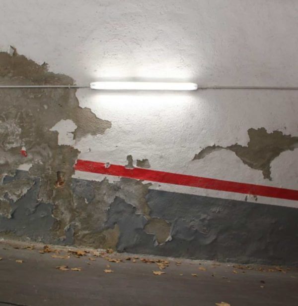 Pintura descascarada en una pared con una raya roja, bajo una luz fluorescente.