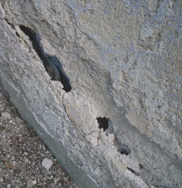 Primer plano de una superficie de piedra gris desgastada con grandes grietas y agujeros.