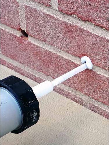 Pistola de calafateo rellenando una grieta en una pared de ladrillos rojos.