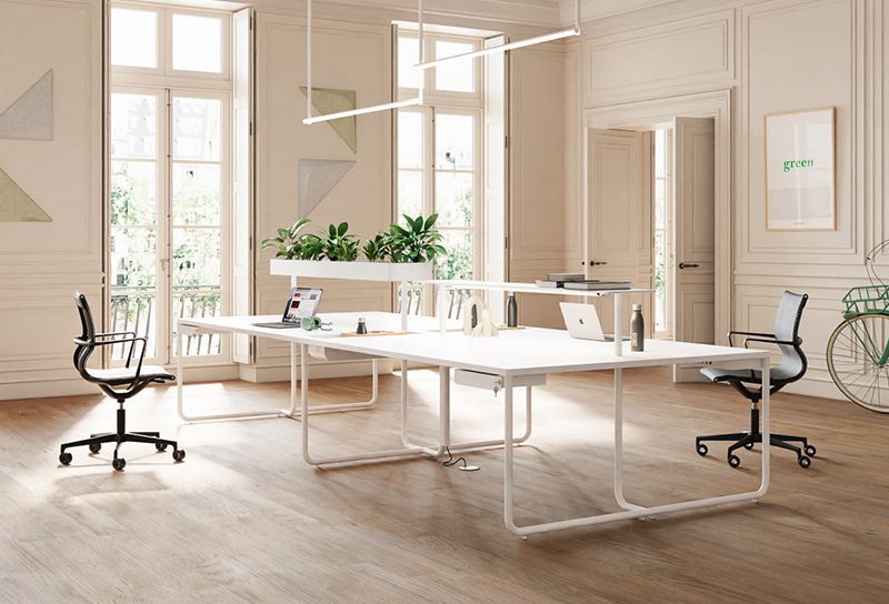 Une personne sur un échafaudage installe un luminaire dans une pièce de style industriel avec des conduits apparents et des suspensions lumineuses.