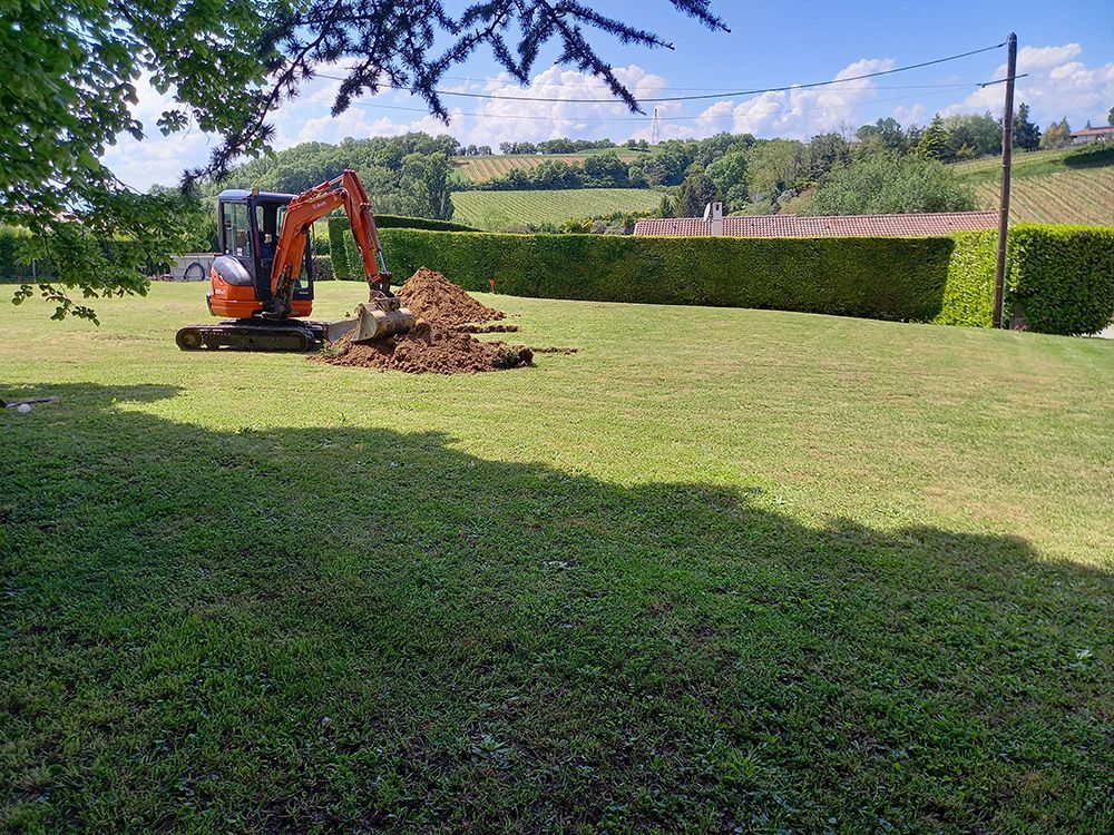 Une tranchée dans la terre avec des tuyaux gris pour la construction ; un baril blanc en arrière-plan.