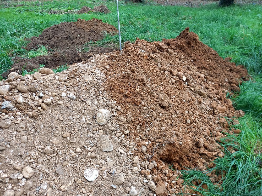 Tas de terre de différentes couleurs et textures sur un sol herbeux ; un piquet se dresse dans le tas.