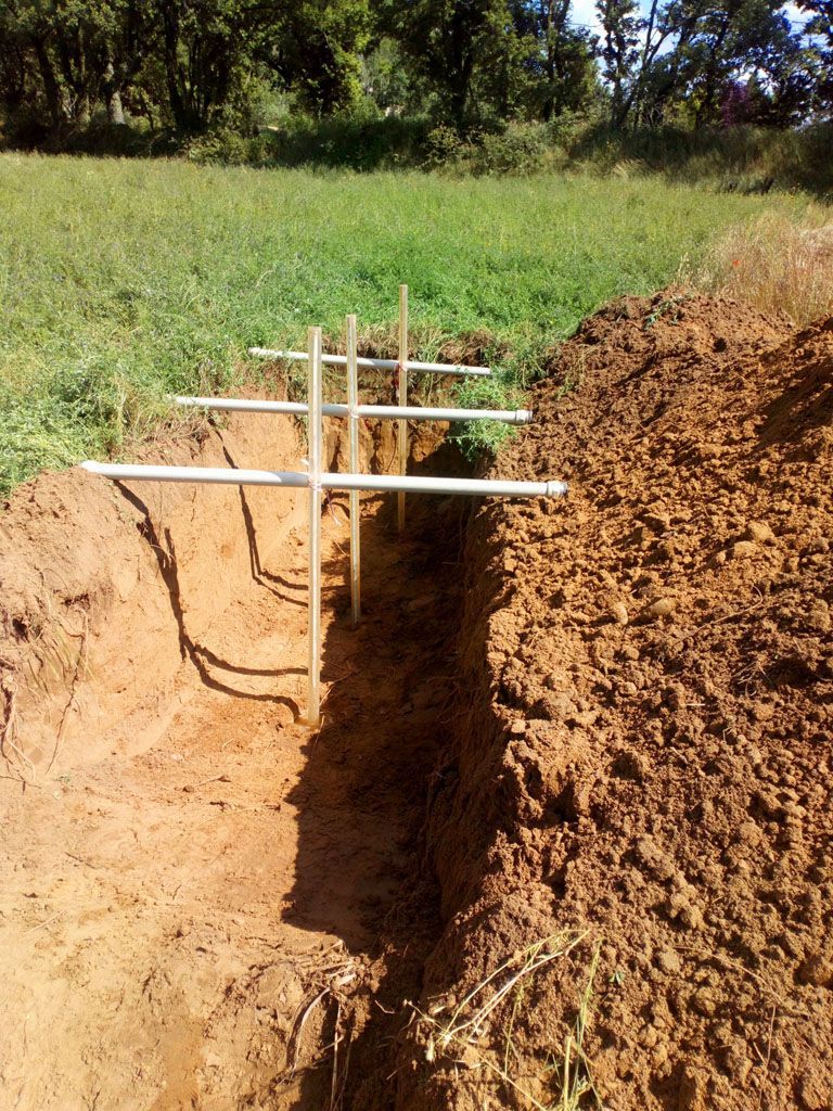 Tranchée creusée dans la terre brune avec des tuyaux gris posés dessus pour un projet de construction.